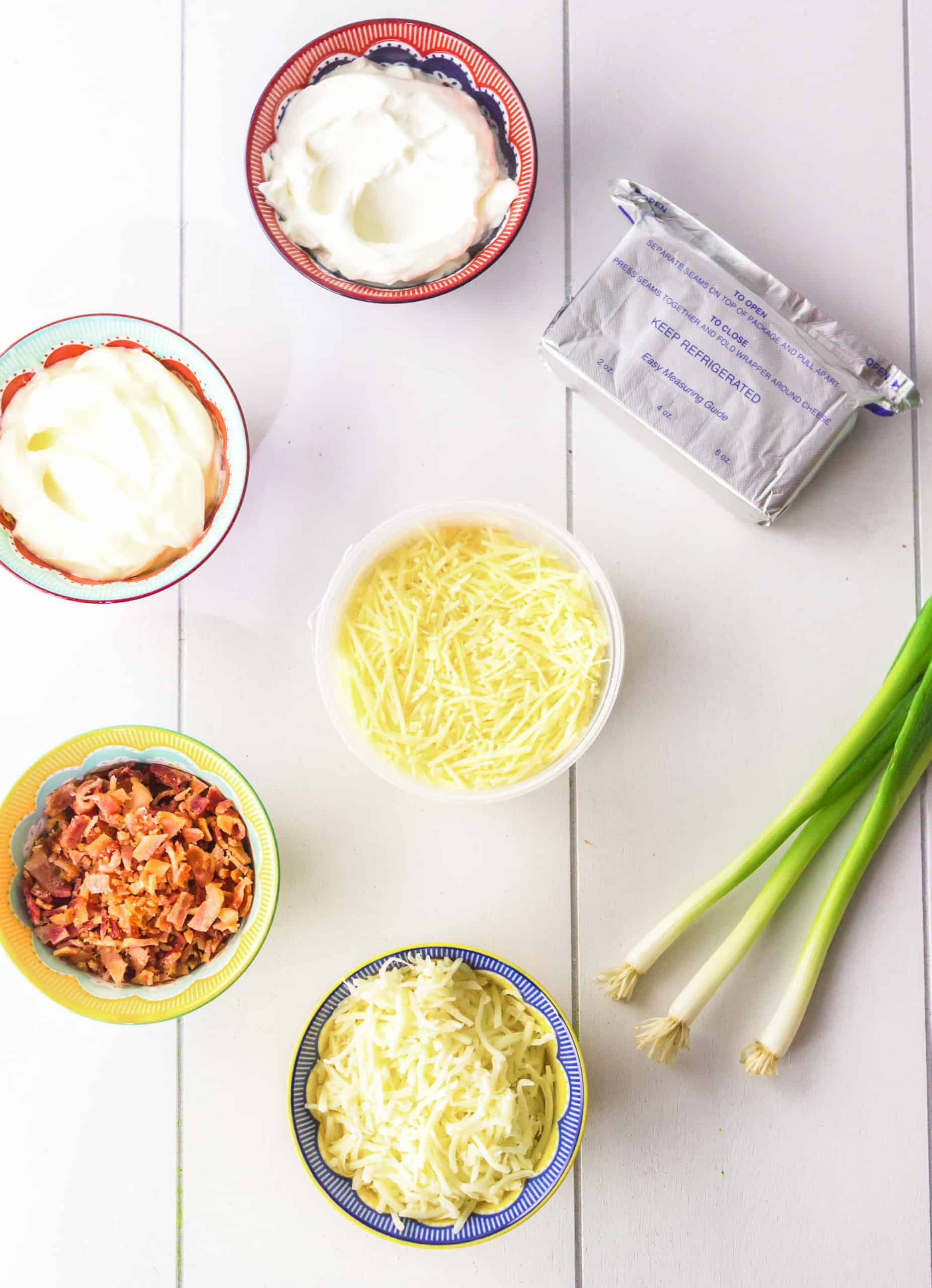 ingredients for baked cheese dip including cream cheese, mayo, sour cream, shredded cheese, bacon and chives