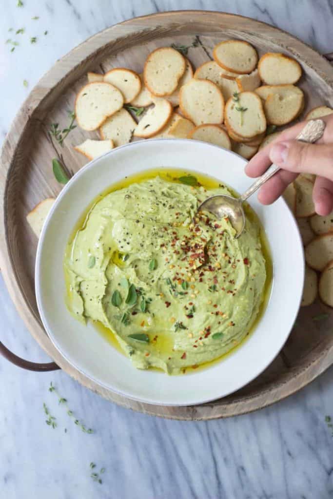 overhead photo of whipped avocado white bean dip with vegan melba toast dippers