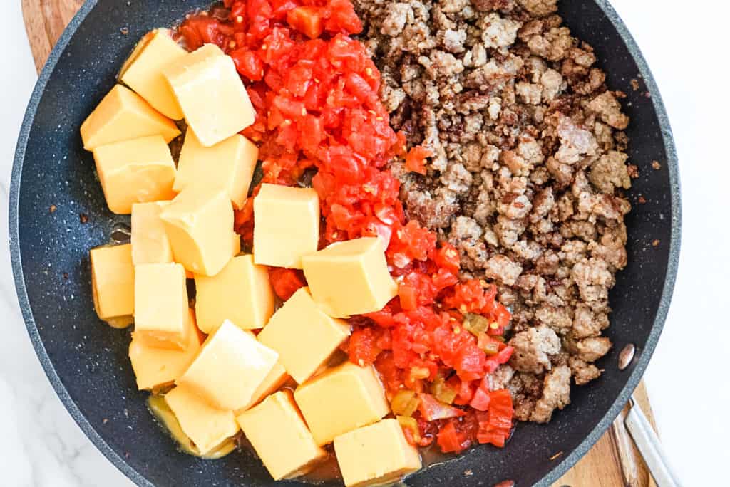 large skillet with cooked sausage, rotel tomatoes and velveeta cheese cubes 