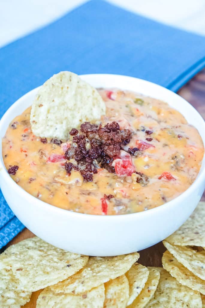 Prepared Rotel Dip in a white bowl garnished with cooked sausage and served with tortilla chips on the side.