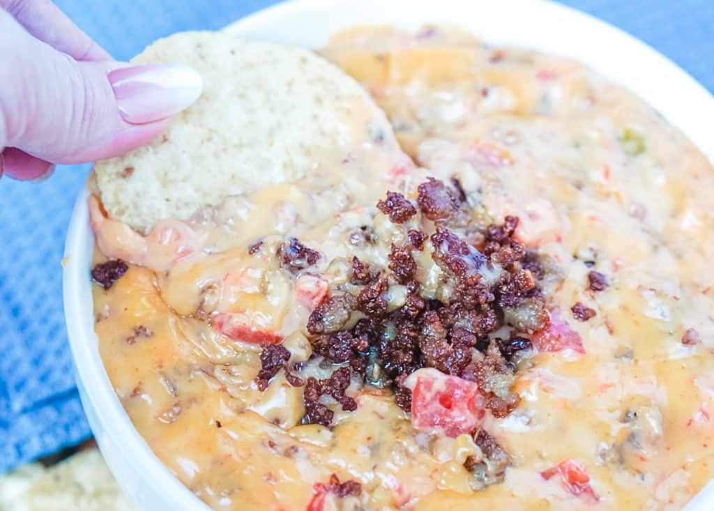 Tortilla chip being dipped into Rotel Dip with sausage