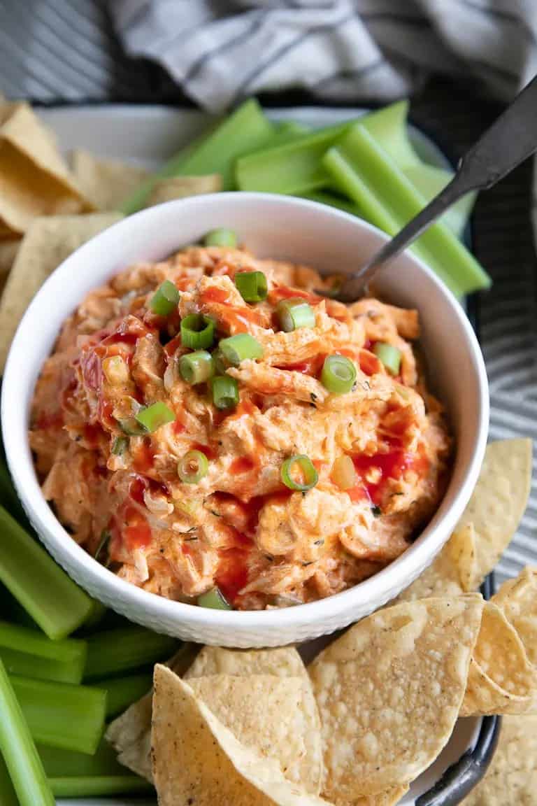 crockpot buffalo chicken dip in a white bowl with tortilla chips and celery dippers