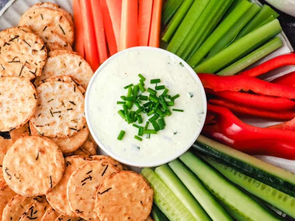 sour cream dip in a bowl surrounded by carrots, celery and crackers for dipping