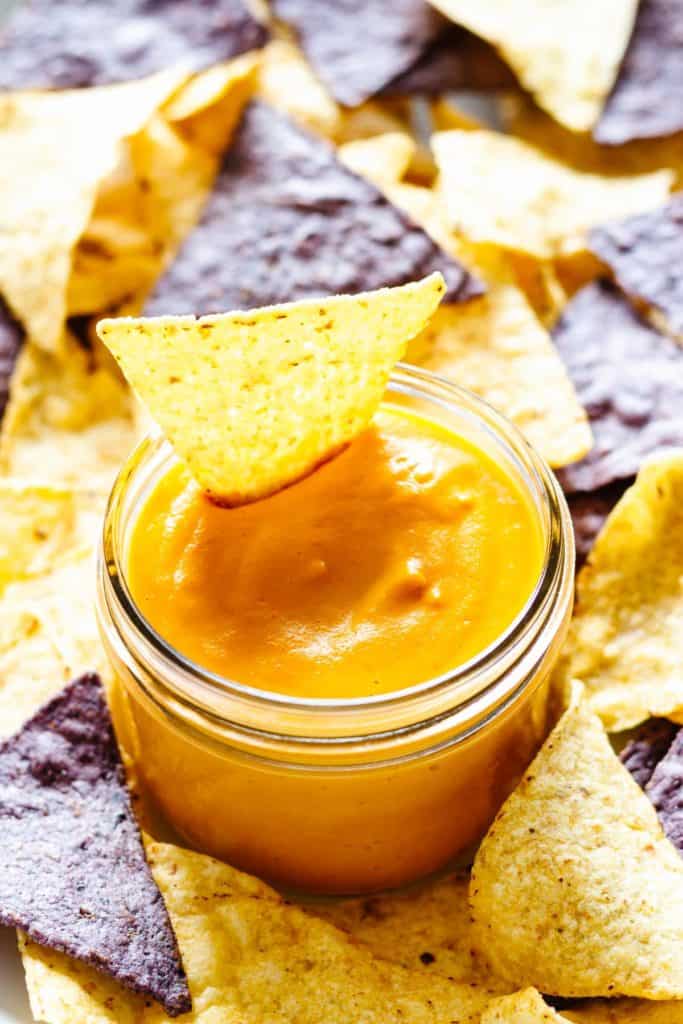 vegan nacho cheese dip in a jar with tortilla chips on the side