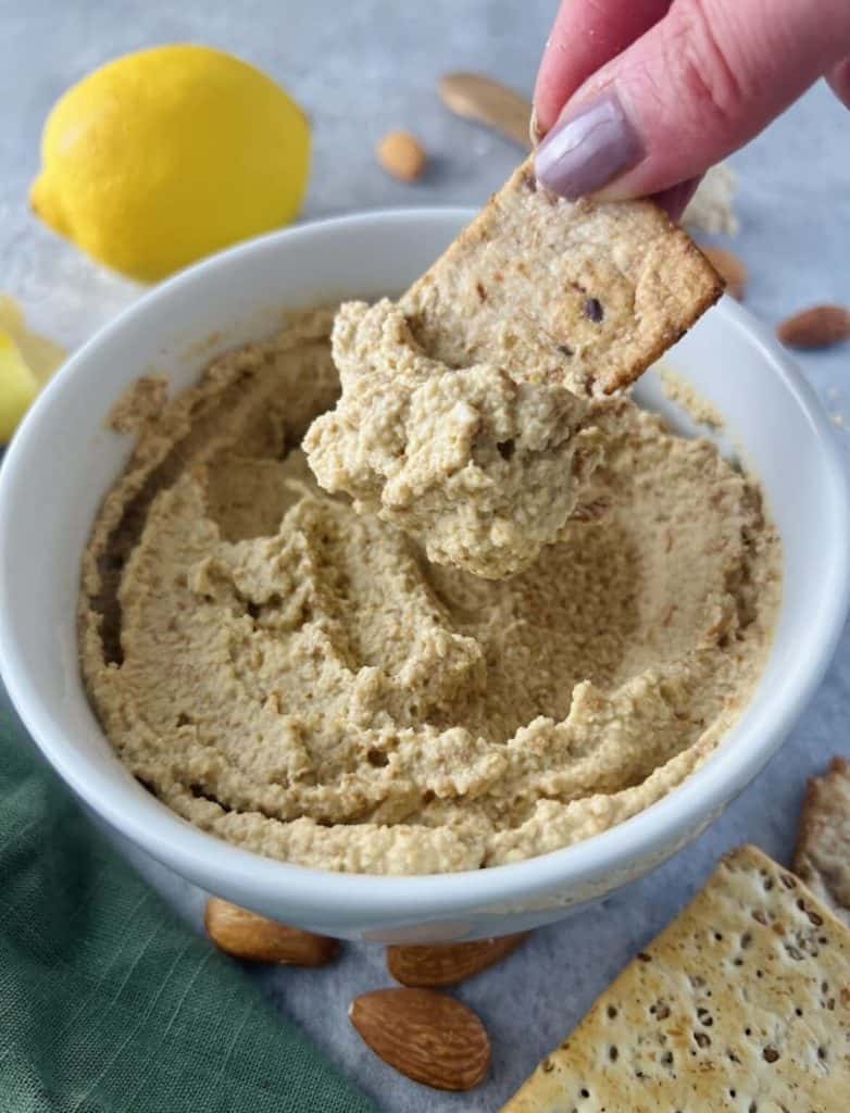 vegan cracker being dipped into creamy almond dip aka bitchin' sauce copycat
