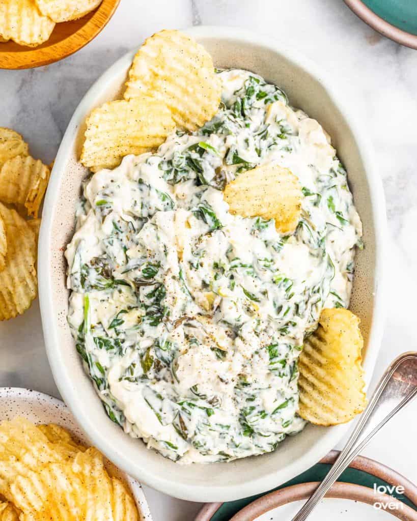 large casserole of crockpot spinach artichoke dip with potato chips on the side