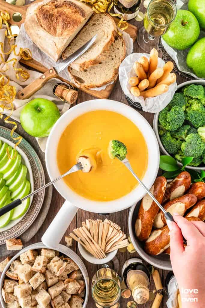 cheese fondue in a white fondue pot surrounded by different dippers