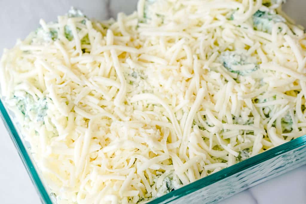 uncooked spinach dip in a baking dish topped with mozzarella cheese