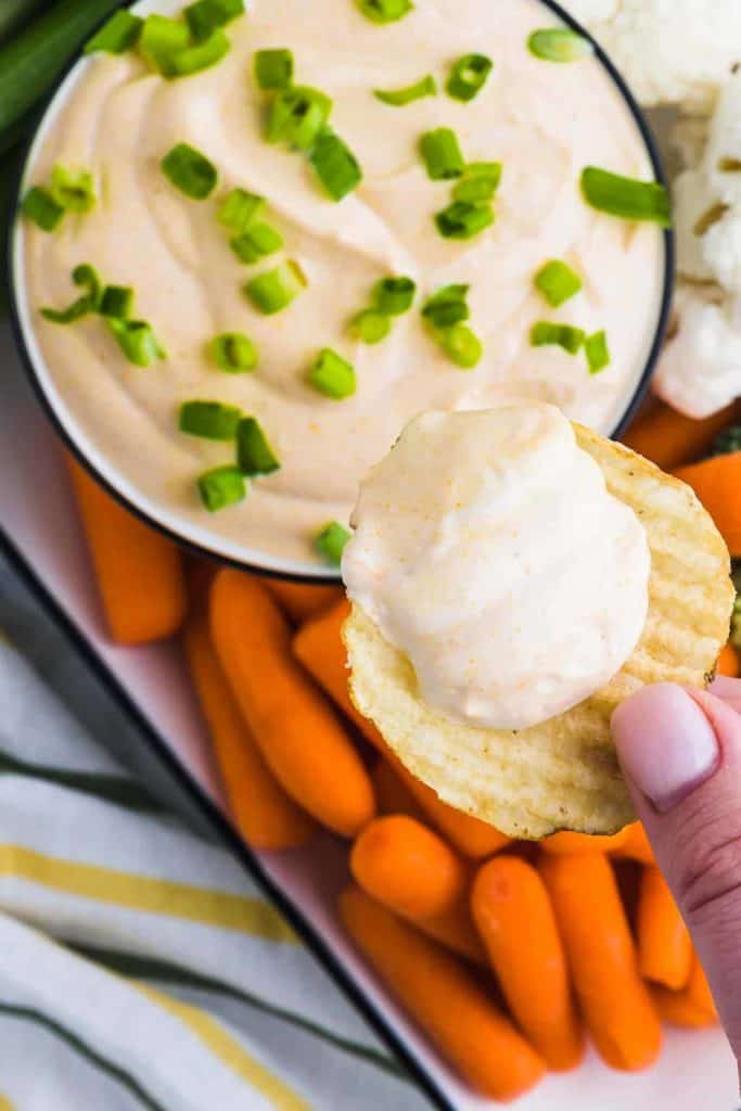 Ruffles potato chip being dipped into curry dip with baby carrots on the side