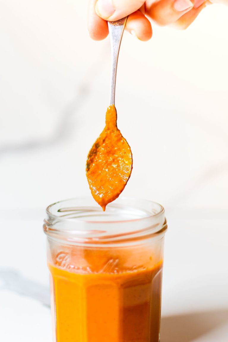 homemade buffalo sauce dripping from a spoon into a jar