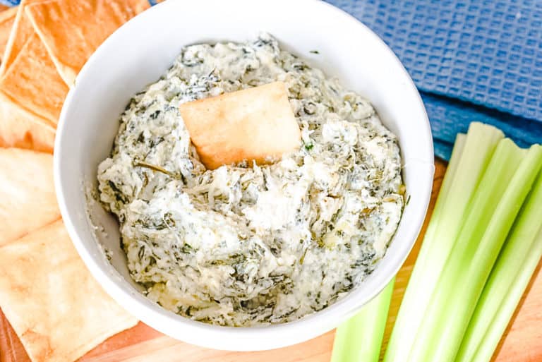 spinach dip in a white bowl with celery and pita chips on the side