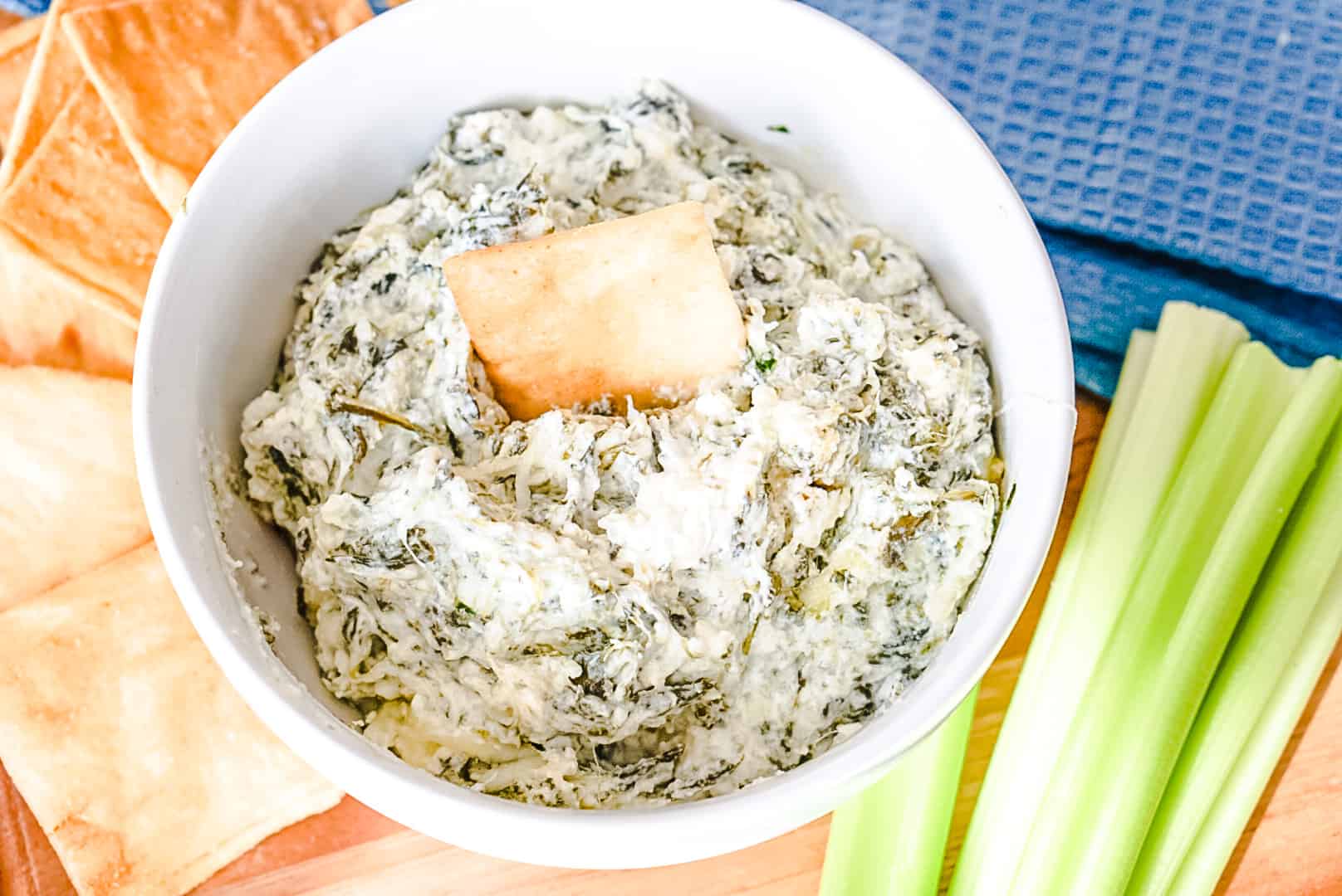 spinach dip in a white bowl with celery and pita chips on the side