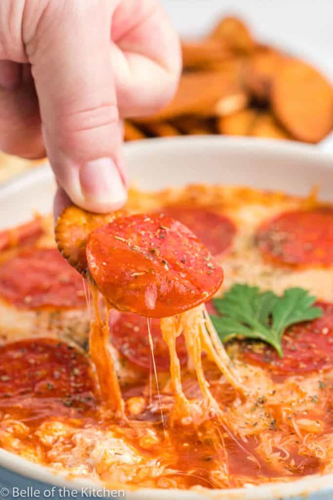 cracker being dipped into pepperoni pizza dip