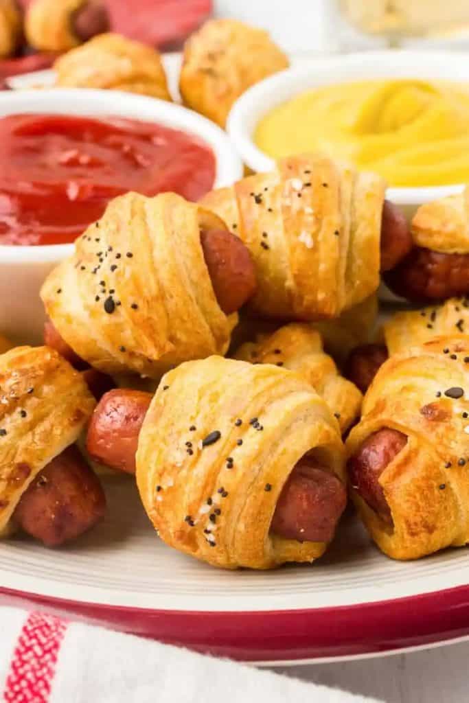 pigs in a blacked stacked on a plate with dipping sauce on the side