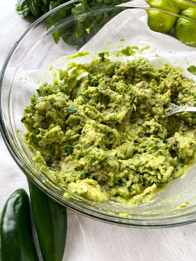 mashed guacamole without tomatoes in a clear bowl with a fork