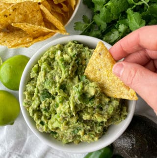 tortilla chip being dipped in guacamole without tomatoes
