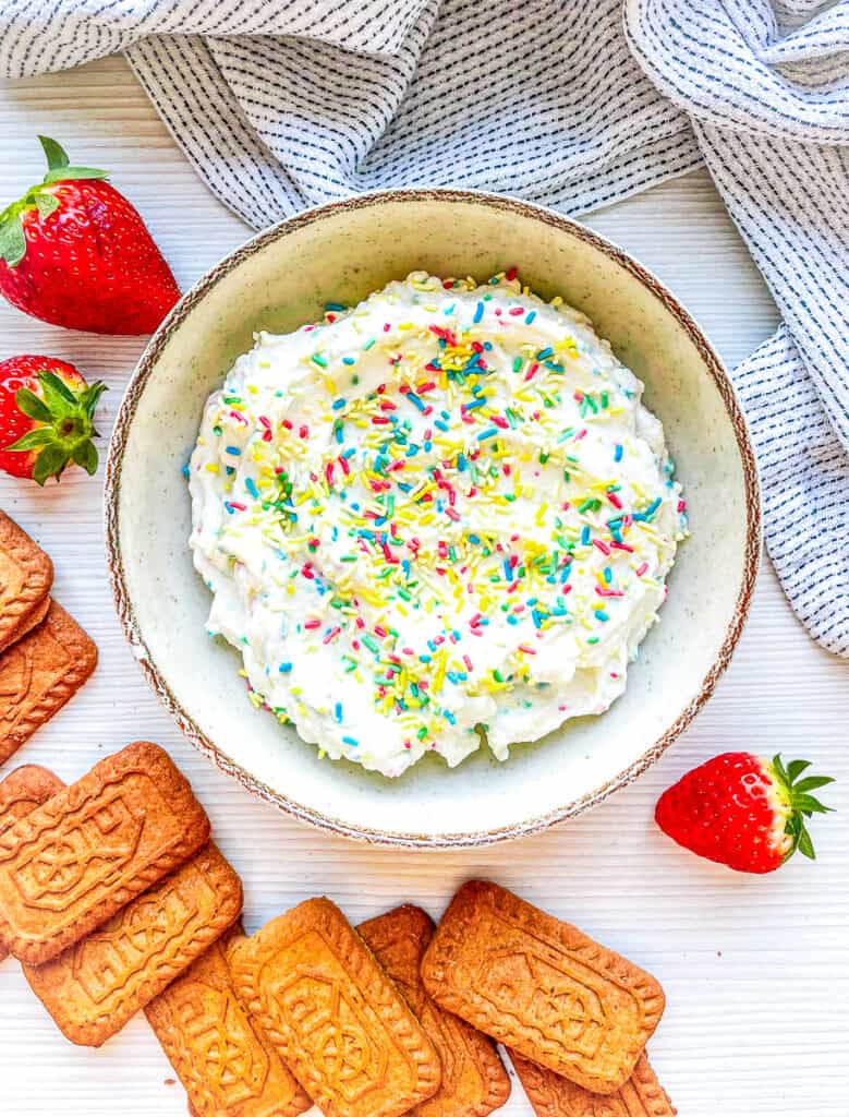 cake batter dip with colorful candy sprinkles surrounded by cookies and strawberries