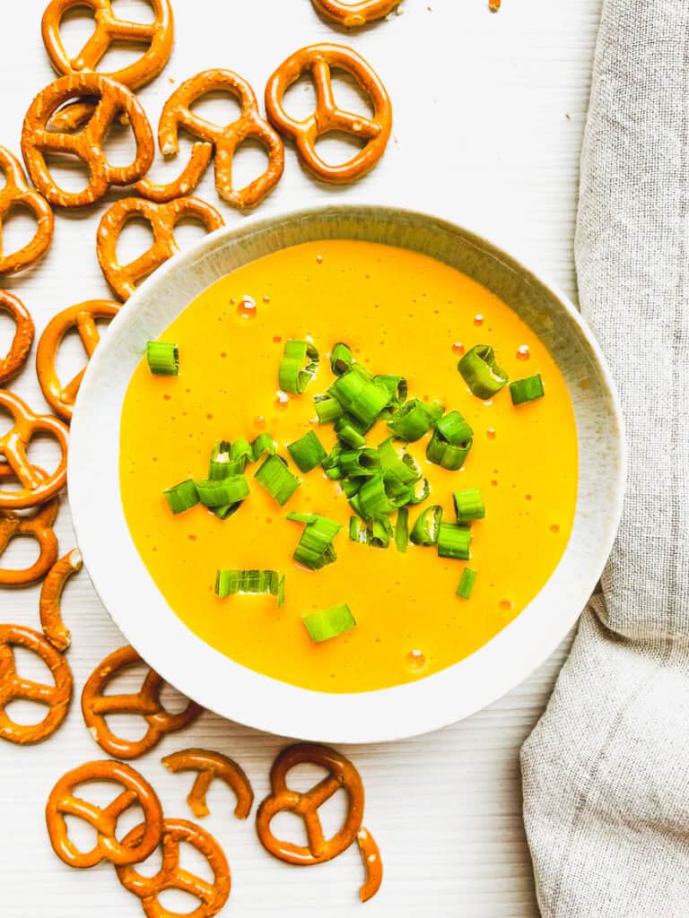 beer cheese dip in a bowl with scallions and pretzels on the side for dipping