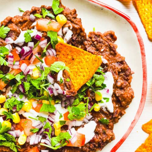 black bean dip loaded with toppings including sour cream, tomatoes, onion, corn and cilantro