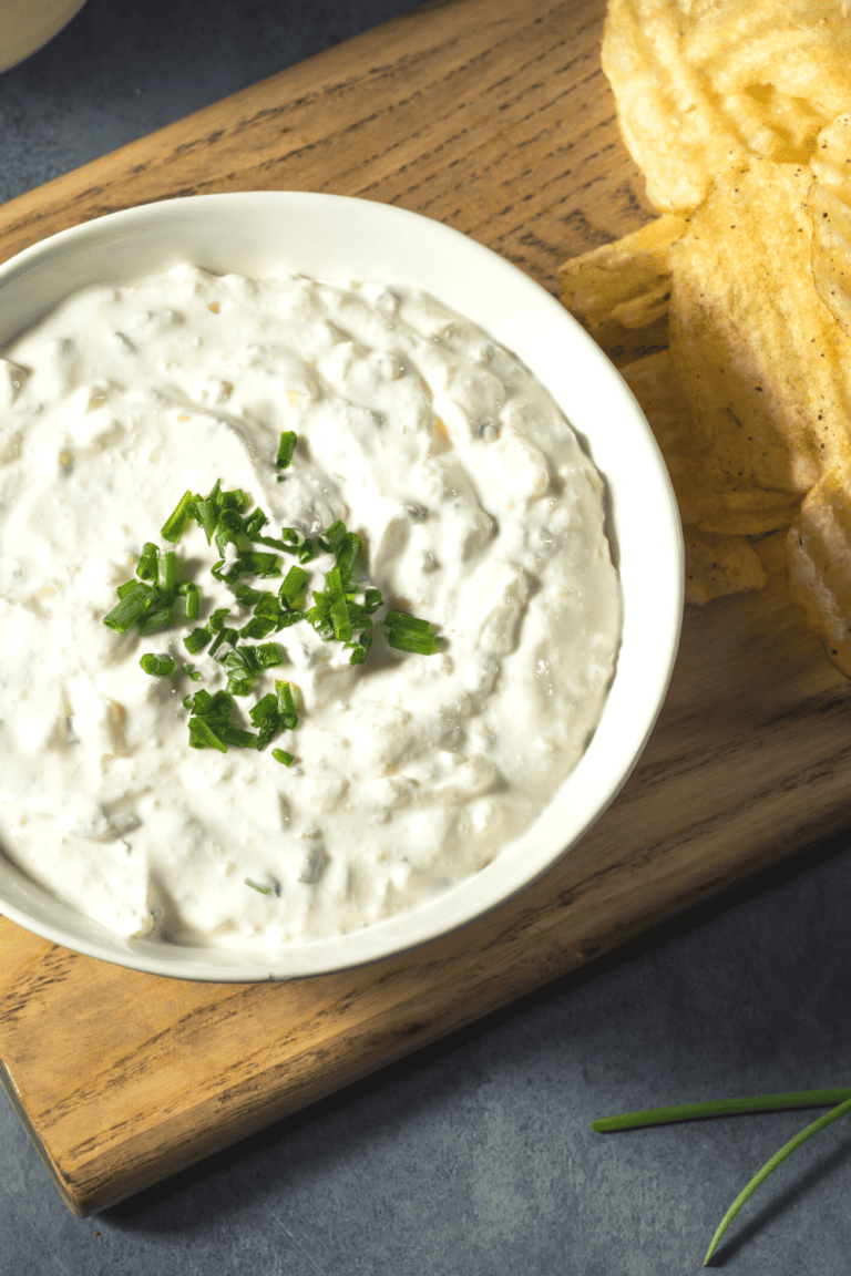 onion dip in a bowl on a cutting board with a side of potato chips