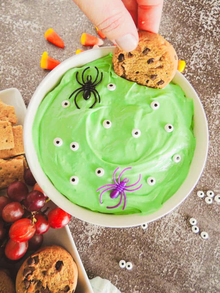 chocolate chip cookie being dipped in green Halloween dessert dip with edible candy eyes