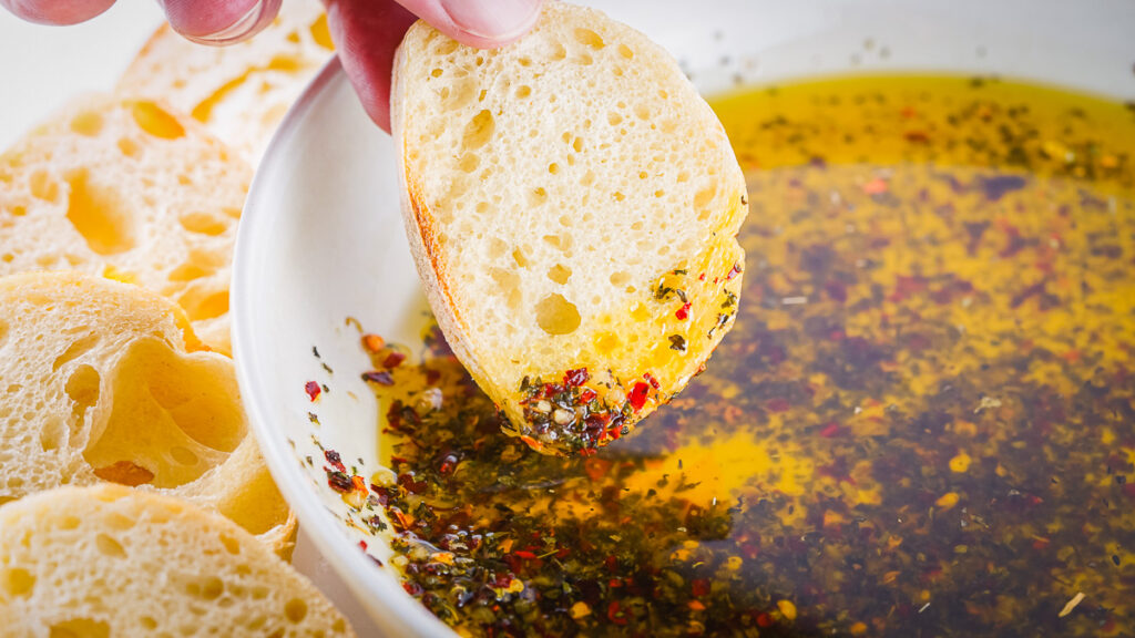 baguette slice being dipped into bread dipping oil with spices