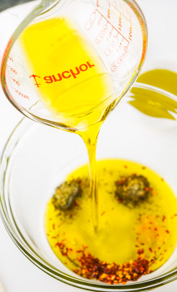 extra virgin olive oil being poured on spices to make bread dipping oil