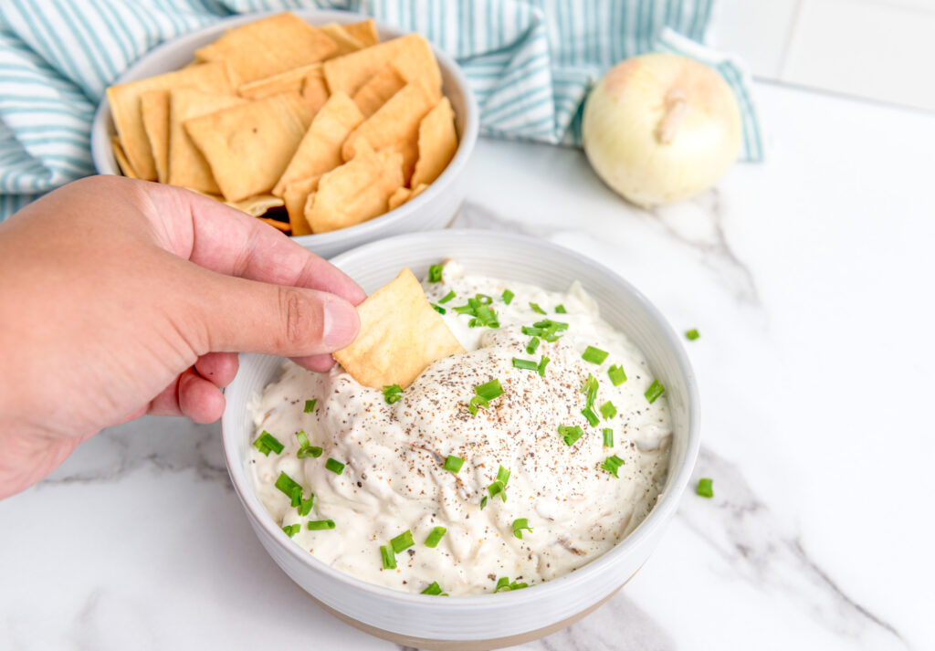 pita chip being dipped into homemade onion dip made with caramelized onions