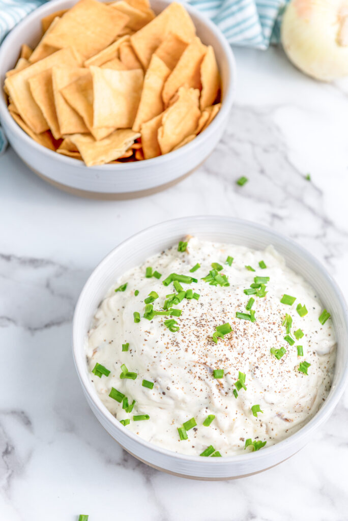 fully prepared caramelized onion dip in a white bowl garnished with chives and a side of pita chips