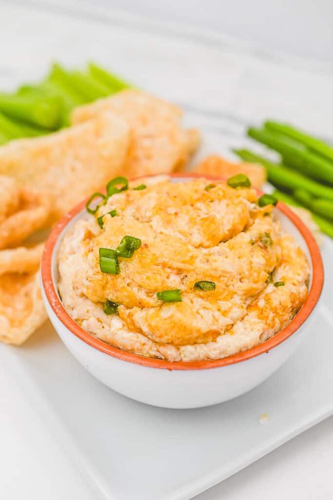 crab rangoon dip in a bowl garnished with green onions and pork rinds on the side for dipping