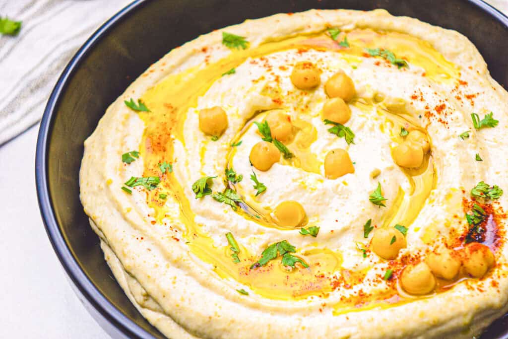 authentic hummus recipe with classic hummus flavor served in a black bowl with olive oil drizzle