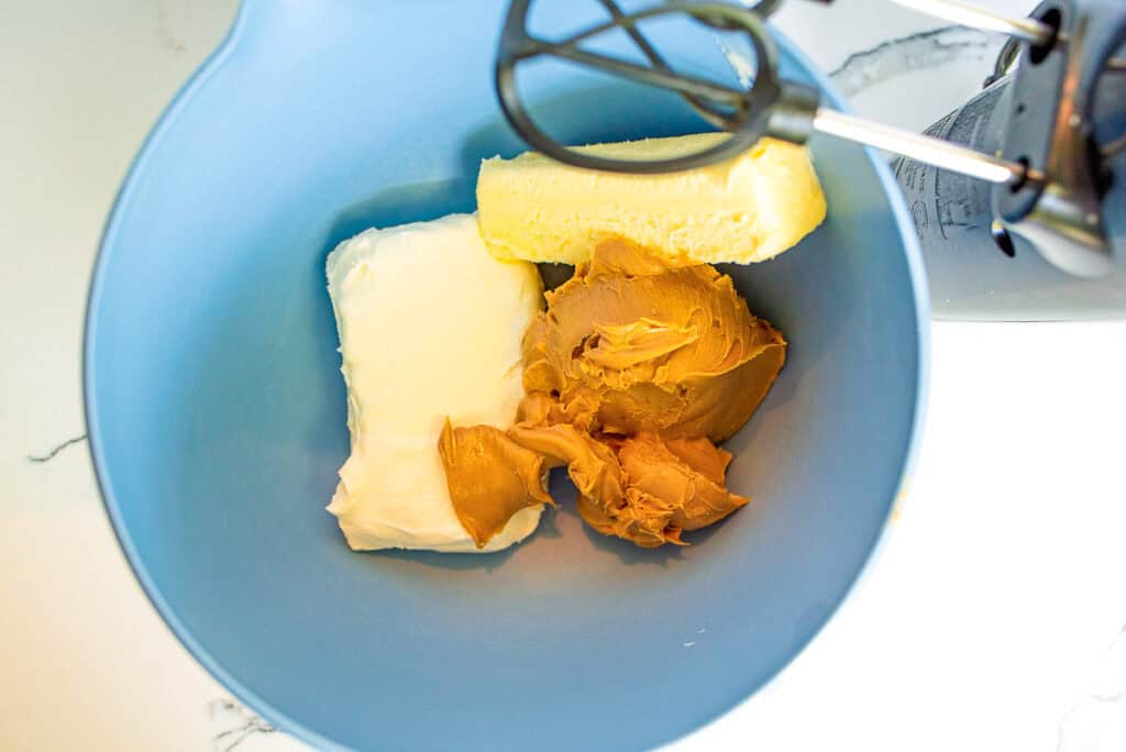 hand mixer getting ready to mix butter, cream cheese, and peanut butter in a. bowl