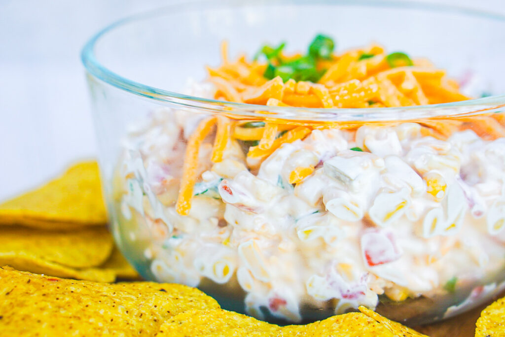 Side view of corn dip with rotel in a clear glass bowl with tortilla chips