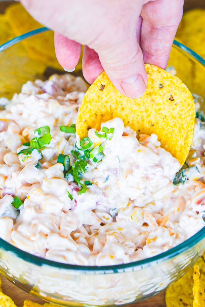 tortilla chip being dipped in prepared corn dip with rotel