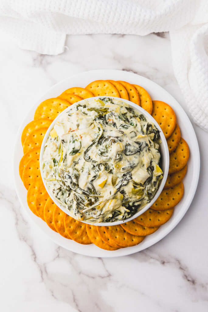 overhead shot of crockpot spinach artichoke dip with butter crackers around the bowl