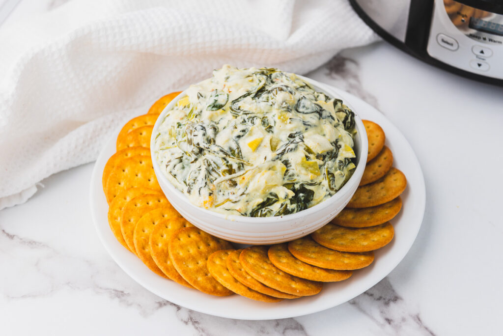 finished crockpot spinach and artichoke dip with crackers on the side for dipping