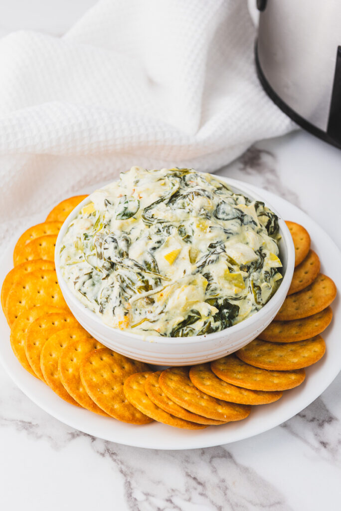 warm crockpot spinach artichoke dip in a bowl ready to eat with crackers