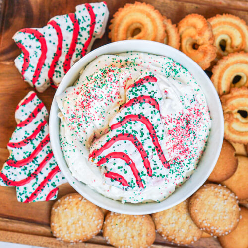 Little Debbie Christmas Tree Dip in a bowl with holiday sprinkles, surrounded by cookies and Little Debbie Christmas Tree Cakes.
