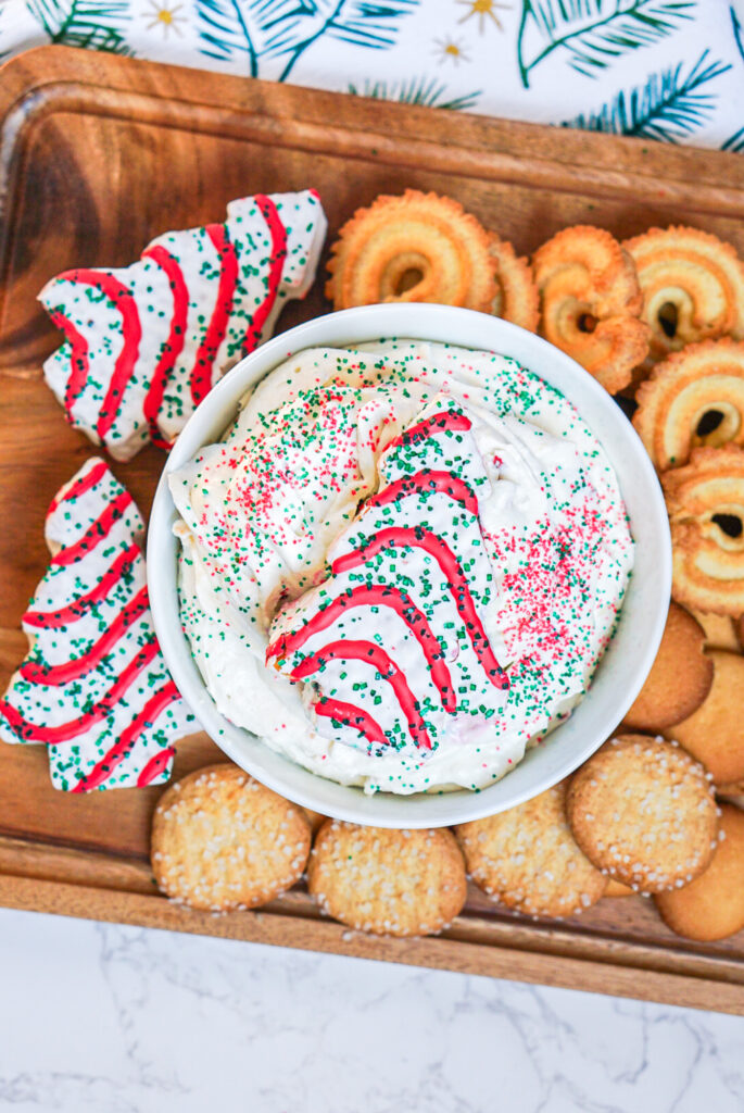 Little Debbie Christmas tree cake dip in a white bowl with red and green sprinkles and cookies