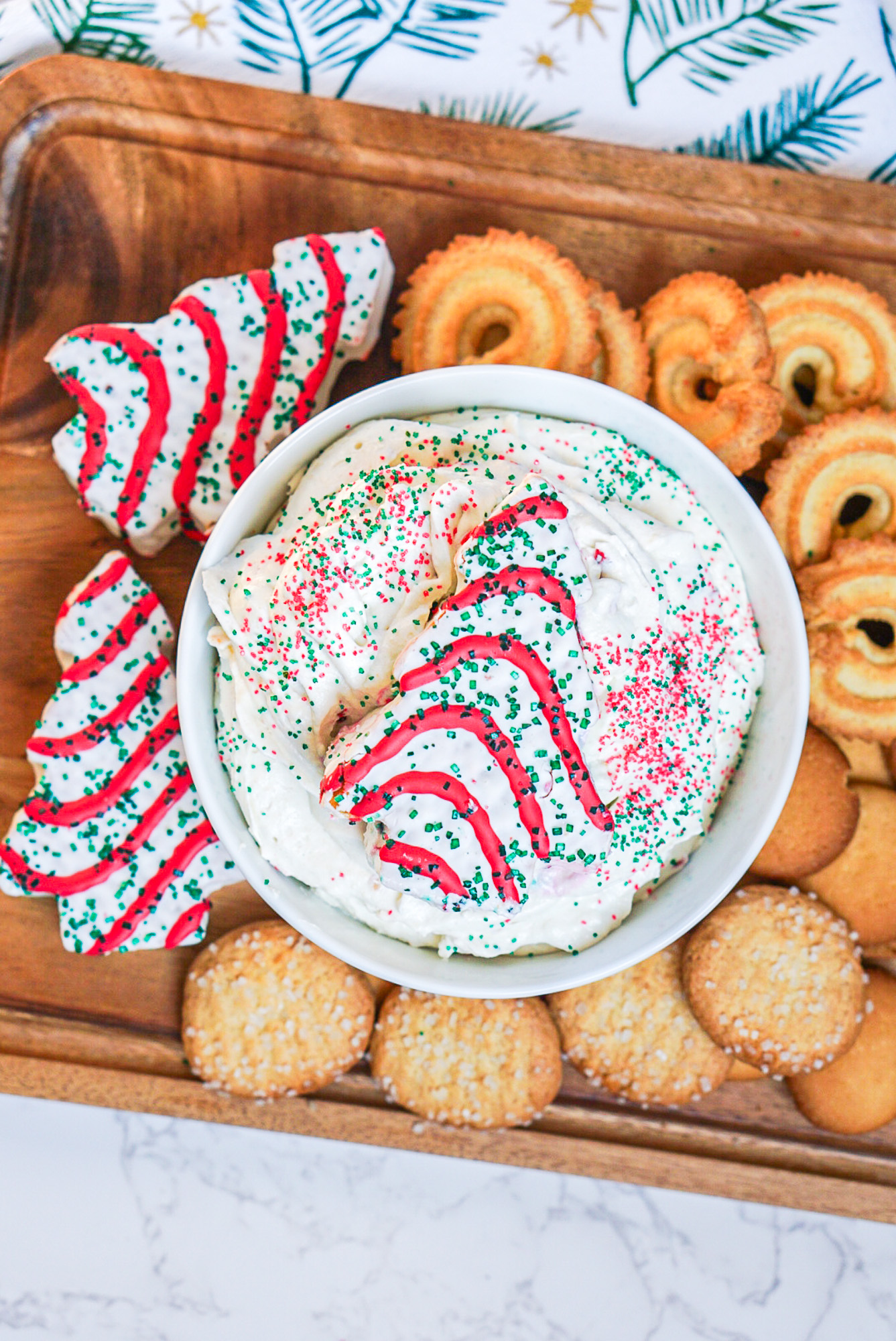Little Debbie Christmas Tree Dip in a bowl with holiday sprinkles, surrounded by cookies and Little Debbie Christmas Tree Cakes.