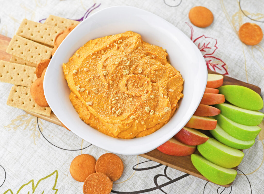 prepared pumpkin pie dip in a white bowl with graham crackers, nilla wafers and apple dippers