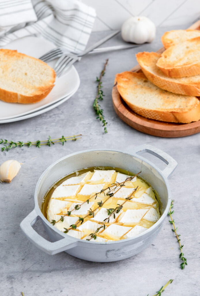 fully prepared baked brie with honey, garlic and rosemary with baguettes on the side