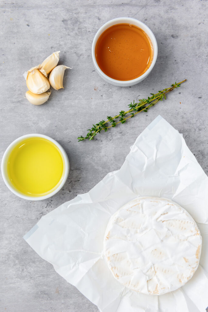 ingredients for baked brie with honey including brie cheese wheel, honey, garlic, olive oil and rosemary sprigs