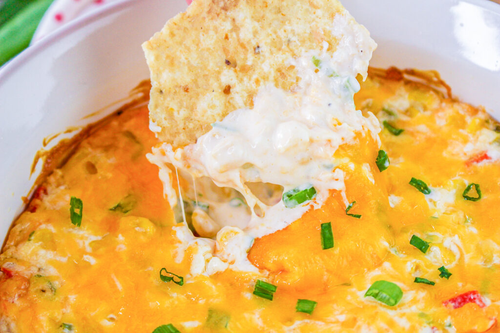 tortilla chip being dunked in hot corn dip with creamy melty cheese