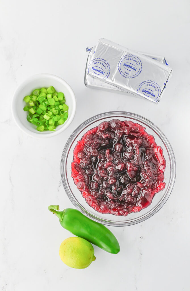 ingredients for cranberry jalapeno cream cheese dip including whole cranberry sauce, cream cheese, jalapeno, lime and green onions
