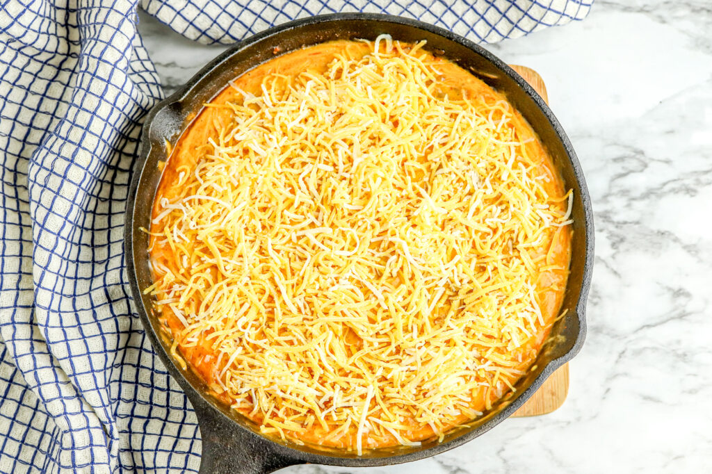 shredded cheese on top of melted chili cheese mixture in cast iron skillet