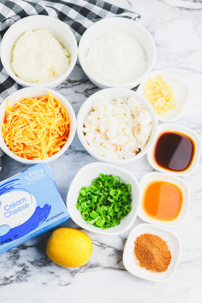 all the ingredients laid out on a counter for cajun crab dip including lump crab meat, cream cheese, cheddar, mayo, lemon, creole seasonings and more
