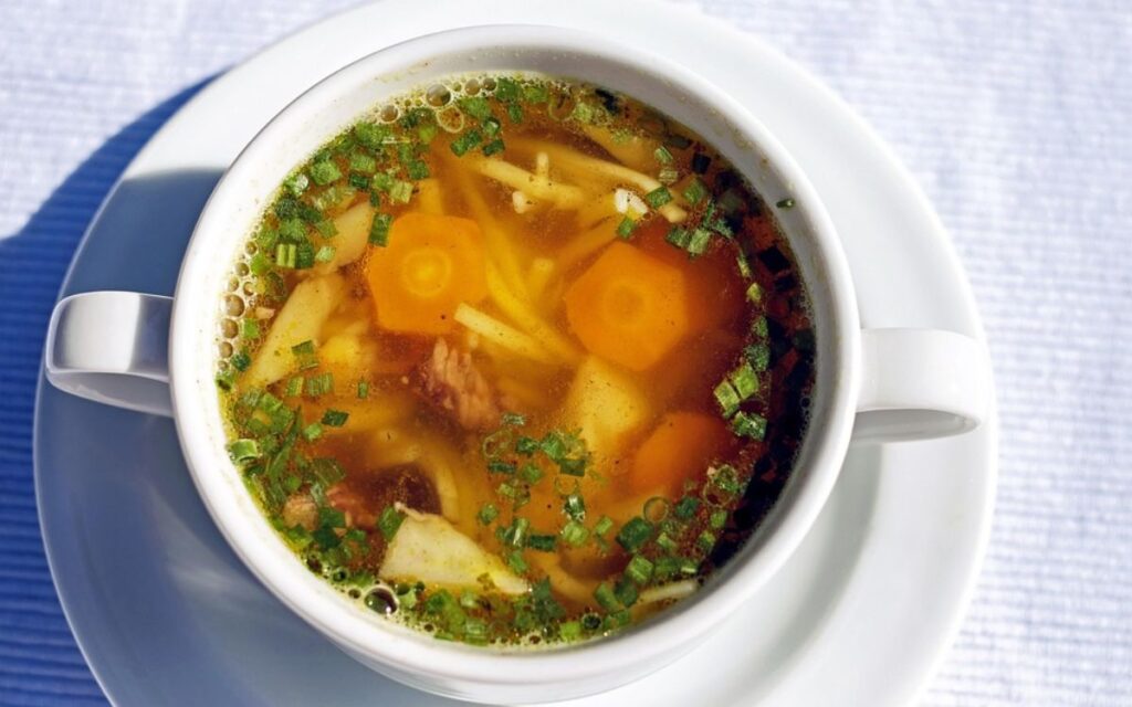 Cup of clear vegetable soup with carrots, potatoes, and herbs