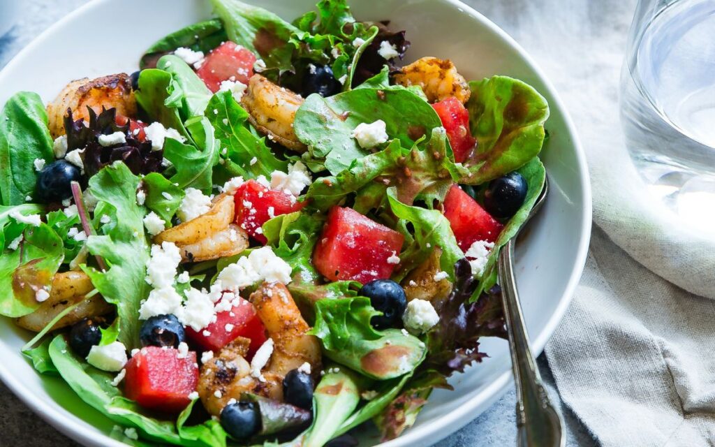 A fresh salad with leafy greens, shrimp, watermelon, blueberries, and crumbled feta cheese