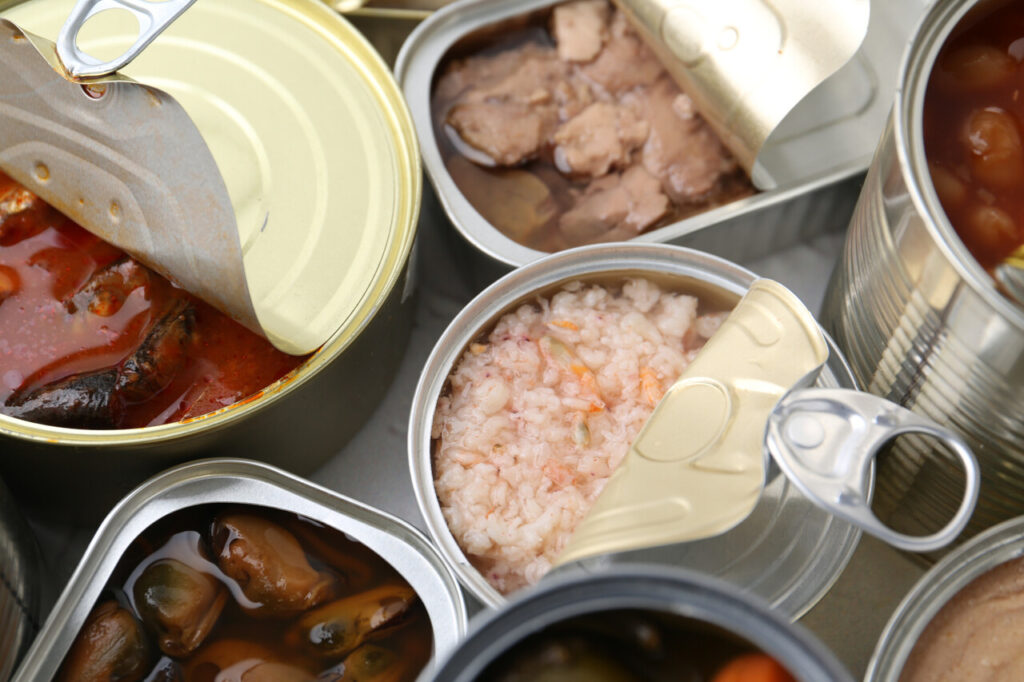 Open tin cans with different preserved products on table, closeup